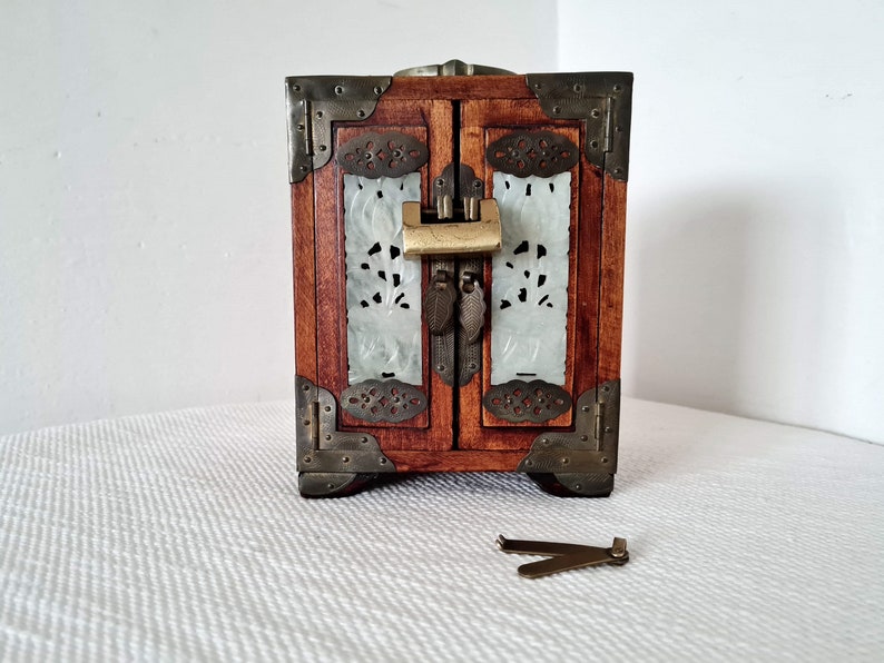 May include: A small wooden jewelry box with a carved white jade front and brass accents. The box has a lock and key.