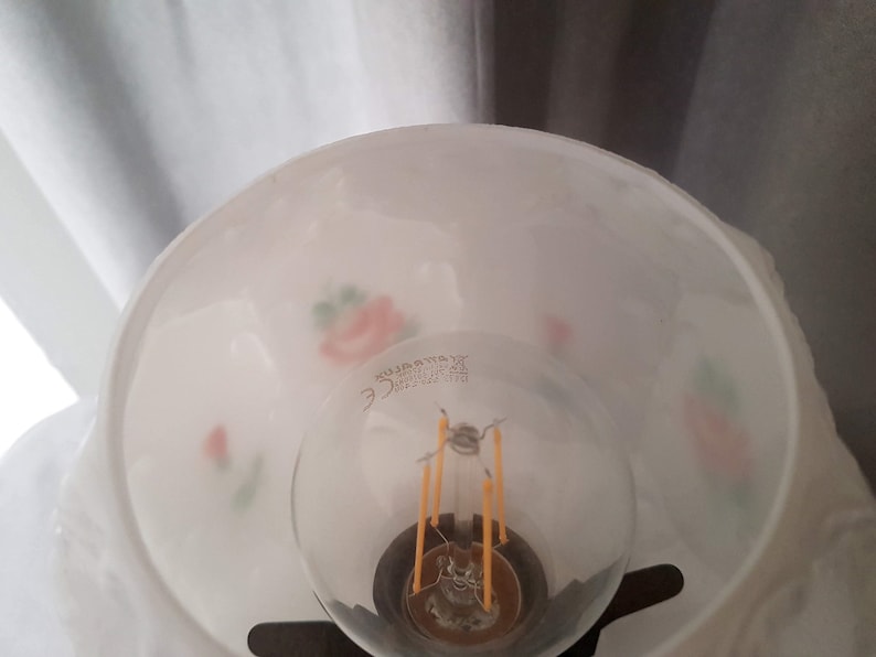 May include: White lampshade with a floral design and a light bulb inside. The lampshade has a small sticker on the bottom that reads "Made in China".