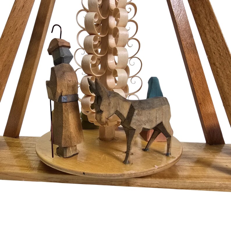 May include: A wooden Christmas pyramid with a carved donkey, a figure of a man with a staff, and a stylized tree with a spiral design.