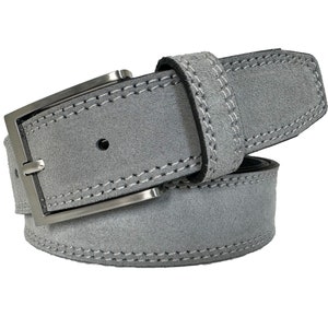 Peut inclure: Une ceinture en daim gris avec une boucle argentée et des coutures blanches. La ceinture est pliée en deux et la boucle est visible.