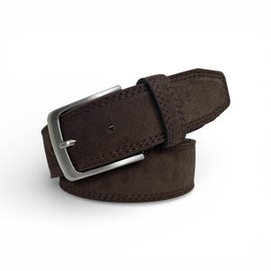 May include: A brown suede belt with a silver-colored buckle. The belt is made of a soft, textured material and features detailed stitching along the edges. The buckle is rectangular and has a classic design.