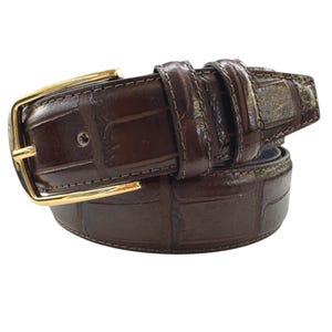 Op de afbeelding: Een bruine leren riem met een gouden gesp. De riem heeft een krokodilpatroon.