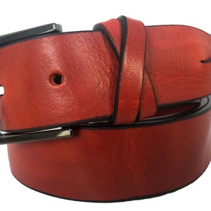 Op de afbeelding: Een rode leren riem met een zilveren gesp. De riem is dubbelgevouwen en de gesp is zichtbaar.