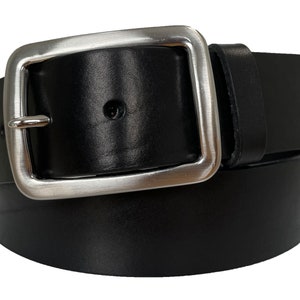 Puede incluir: Un cinturón de cuero negro con una hebilla grande, cuadrada y de color plateado. El cinturón está enrollado sobre sí mismo, mostrando la textura suave del cuero y la hebilla brillante. La hebilla tiene una sola espiga.