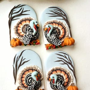 May include: Four Thanksgiving-themed ornaments. Each features a turkey with a colourful tail, a small orange pumpkin, and a tree branch against a light blue backdrop. The turkeys have blue heads and red wattles.