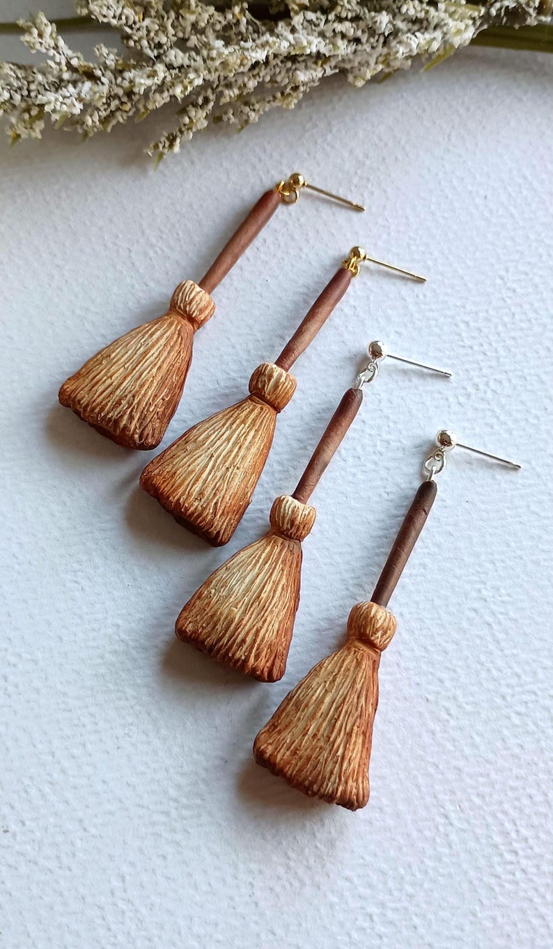 Puede incluir: Un conjunto de tres pendientes de escoba de bruja. Los pendientes est&aacute;n hechos de arcilla polim&eacute;rica marr&oacute;n y beige y tienen pasadores de oro y plata.