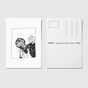 Peut inclure: Carte postale en noir et blanc avec une illustration au stylo d'un masque tenu par des mains. Le verso comporte des lignes d'adresse et le texte "Hughes Maton x MF DOOM".