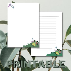 May include: Printable stationery featuring a green frog blowing bubbles with a pink wand. The frog is sitting on a green leaf with purple flowers. The paper has lined writing space.