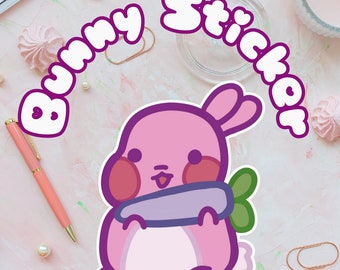 Könnte beinhalten: Ein gestanzter Aufkleber mit einem rosa Cartoon-Hasen mit roten Wangen, der eine violette Karotte mit grünen Blättern hält. Der Text "Bunny Sticker" ist in einer fetten, weißen, abgerundeten Schrift mit dunkelviolettem Rand abgebildet.