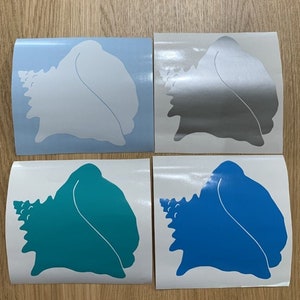 Könnte beinhalten: Vier Muschelförmige Vinyl-Aufkleber in Weiß, Silber, Türkis und Blau. Jeder Aufkleber befindet sich auf einer weißen Rückseite mit abgerundeten Ecken. Die Aufkleber sind quadratisch angeordnet und zeigen die verschiedenen Farboptionen.