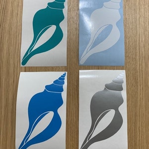 Könnte beinhalten: Vier Muschelförmige Vinylaufkleber in Türkis, Hellblau, Blau und Grau. Jeder Aufkleber hat einen weißen Hintergrund und ein detailliertes Spiraldesign oben. Die Aufkleber sind auf einer hellen Holzoberfläche angeordnet.