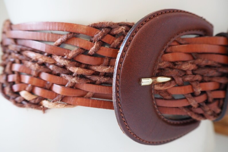 May include: A brown leather belt with a woven design and a large, brown leather buckle.