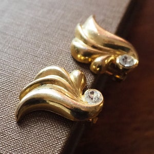 May include: A pair of gold-tone earrings with a leaf design and clear rhinestone accents.