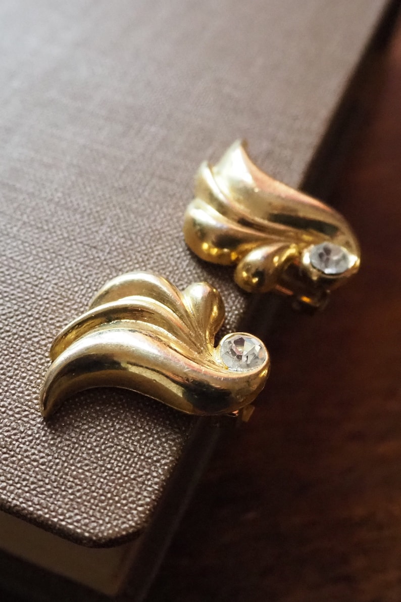 May include: A pair of gold-tone earrings with a leaf design and clear rhinestone accents.