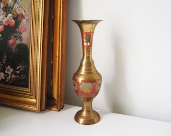 May include: A gold brass vase with intricate floral designs in red, blue, and green. The vase has a wide mouth and a narrow neck, and it stands on a round base.