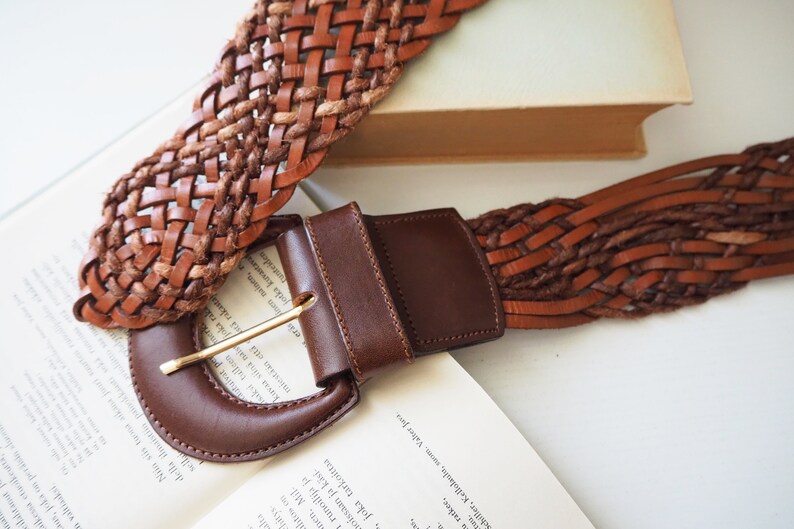May include: A brown leather belt with a woven design and a large, brown leather buckle.