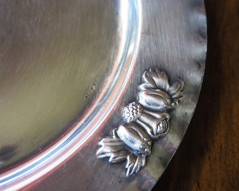 May include: A silver serving dish with a decorative border of grapes and leaves. The dish is marked "ALFI" on the bottom.