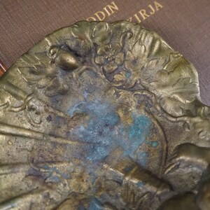 May include: A brass decorative object with a floral design and a small acorn. The object has a patina of green and blue.