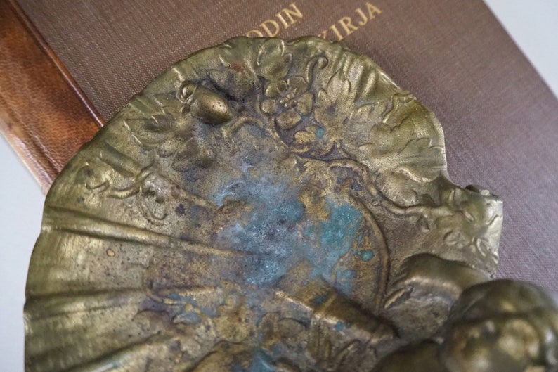 May include: A brass decorative object with a floral design and a small acorn. The object has a patina of green and blue.