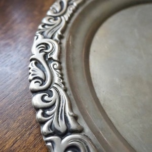 May include: A silver oval serving tray with an ornate, embossed, scroll-like design around the edge.
