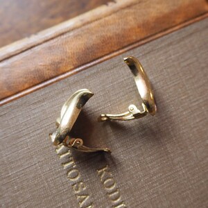 May include: A pair of gold-toned clip-on earrings. The earrings are shaped like a crescent moon and have a simple, elegant design.
