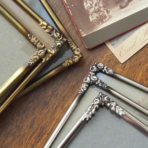 Könnte beinhalten: Nahaufnahme antiker Bilderrahmen mit verzierten floralen Eckdetails. Zwei Rahmen haben eine goldene Oberfläche, während zwei andere silberfarben sind. Eine Vintage-Fotografie und -Karte sind im Hintergrund sichtbar.