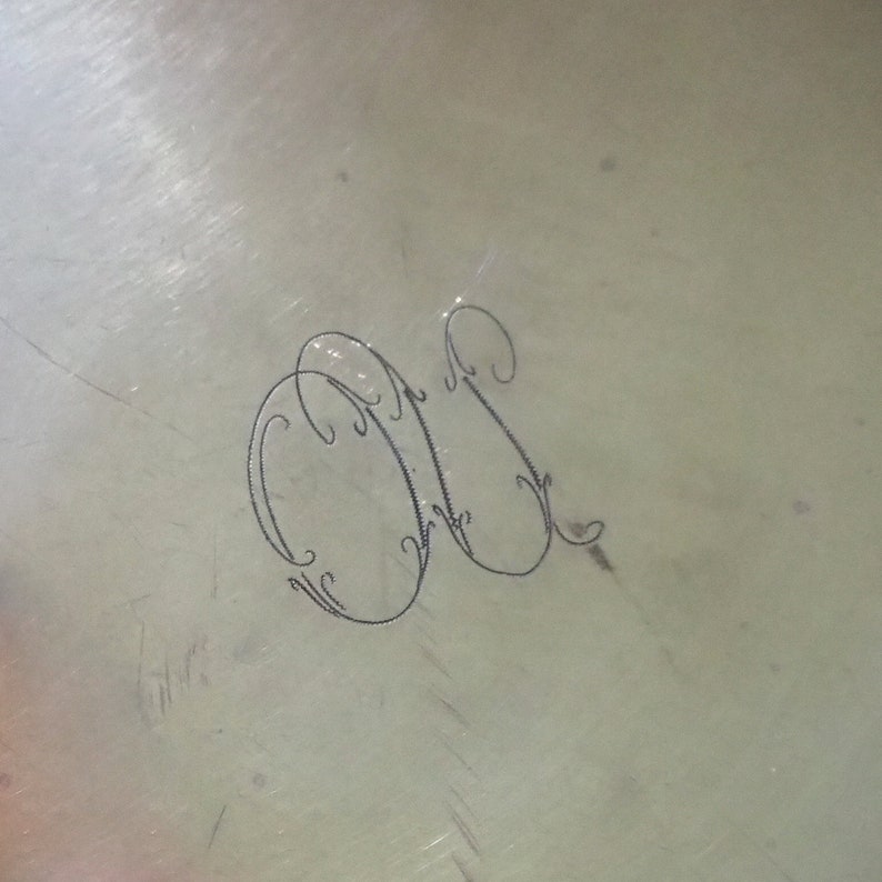 May include: Close-up of a silver surface with an engraved monogram of the letters "M" and "S" in a decorative script.