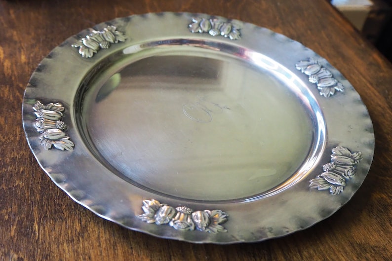May include: A silver serving tray with a decorative border of embossed grapes and leaves.