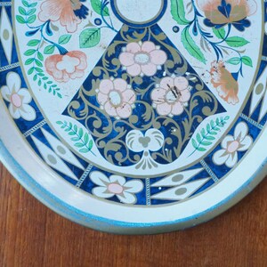 Puede incluir: Una bandeja de servir de metal blanco con un dise&ntilde;o floral azul y dorado. La bandeja tiene un borde azul claro y un fondo blanco con un patr&oacute;n floral azul y dorado.