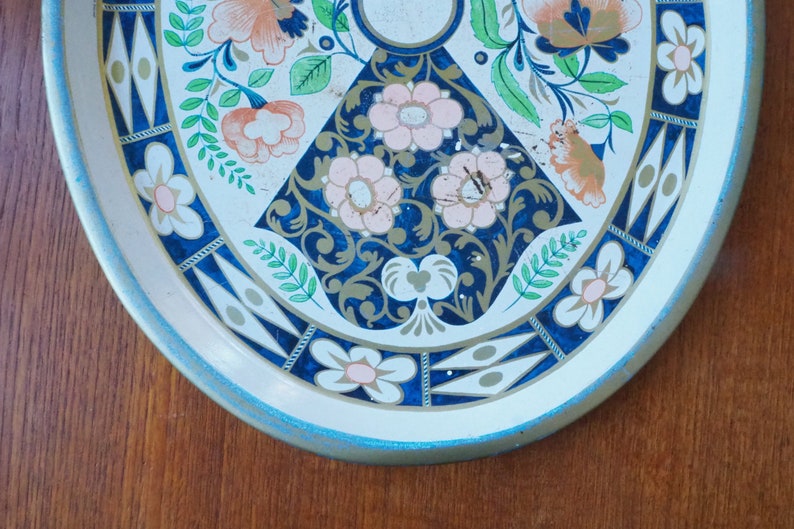 Puede incluir: Una bandeja de servir de metal blanco con un dise&ntilde;o floral azul y dorado. La bandeja tiene un borde azul claro y un fondo blanco con un patr&oacute;n floral azul y dorado.
