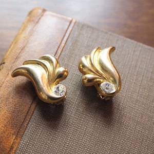 May include: A pair of gold-tone earrings with a leaf design and a clear rhinestone in the center of each earring.