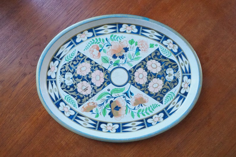 Puede incluir: Una bandeja de servir ovalada de metal con fondo blanco y un dise&ntilde;o floral en tonos azules, rosas y verdes. La bandeja tiene un borde dorado.