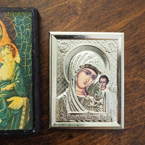 Pu&ograve; includere: Un'icona incorniciata in argento che raffigura la Vergine Maria e il bambino Ges&ugrave;. L'icona ha uno sfondo dorato e il testo "Матерь Божья" in scrittura cirillica.