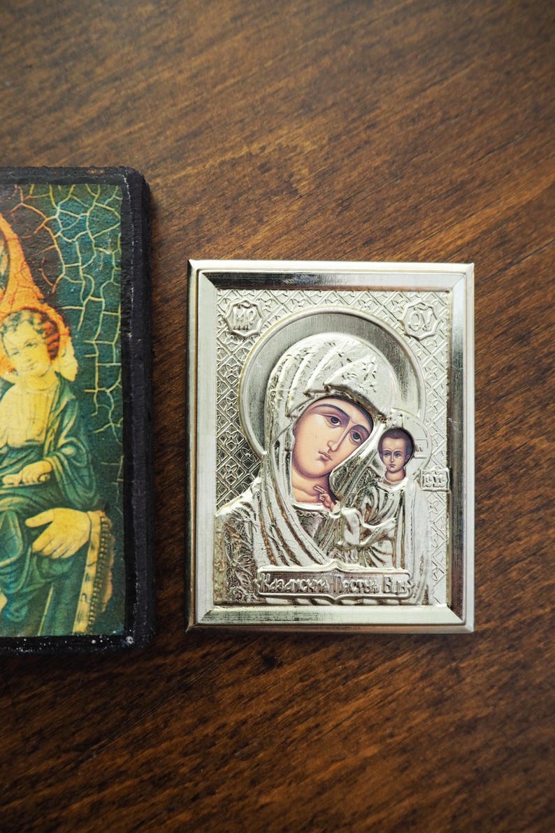 Pu&ograve; includere: Un'icona incorniciata in argento che raffigura la Vergine Maria e il bambino Ges&ugrave;. L'icona ha uno sfondo dorato e il testo "Матерь Божья" in scrittura cirillica.