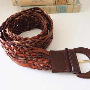 May include: A brown leather braided belt with a large, round, brown leather buckle.