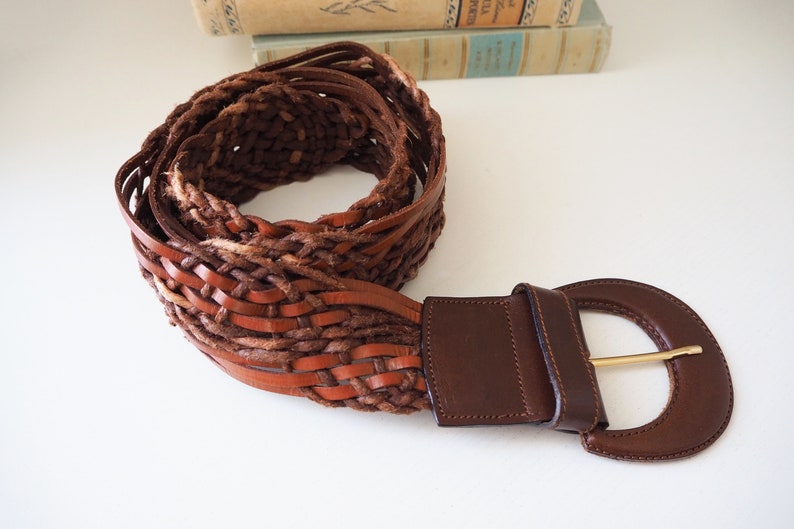 May include: A brown leather braided belt with a large, round, brown leather buckle.