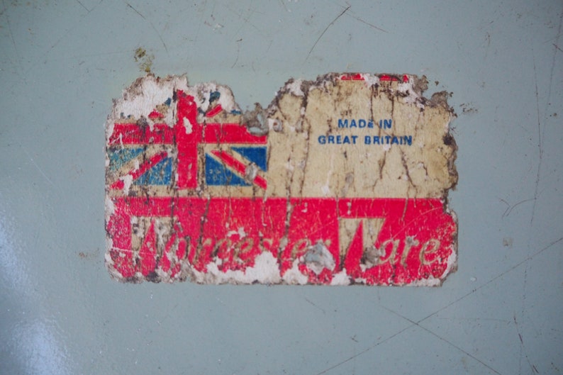 Puede incluir: Una etiqueta vintage roja, blanca y azul con el texto "Made in Great Britain" y una imagen descolorida de la bandera de la Union Jack. La etiqueta est&aacute; parcialmente rasgada y tiene un fondo rojo con la palabra "Ware" en blanco.