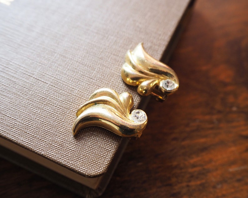 May include: A pair of gold-tone earrings with a leaf design and clear rhinestones.