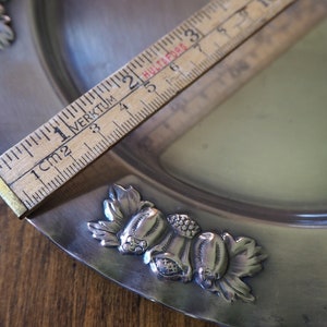 May include: A silver serving dish with a decorative design of leaves and flowers. The dish is approximately 6 inches in diameter.
