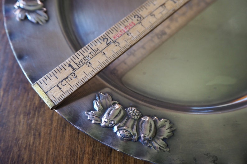 May include: A silver serving dish with a decorative design of leaves and flowers. The dish is approximately 6 inches in diameter.