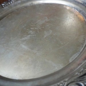 May include: A silver serving tray with a decorative, ornate rim. The tray has a smooth, reflective surface with a faint design in the center.