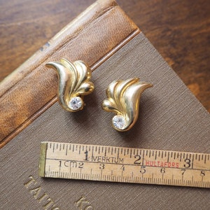 May include: A pair of gold tone earrings with a leaf design and clear rhinestone accents.