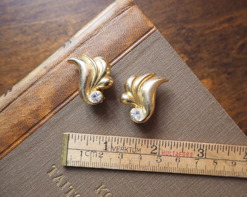 May include: A pair of gold tone earrings with a leaf design and clear rhinestone accents.