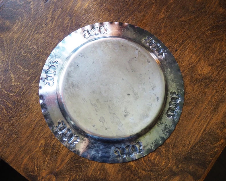 May include: A silver metal serving tray with a decorative embossed border. The tray is round and has a smooth, shiny surface.