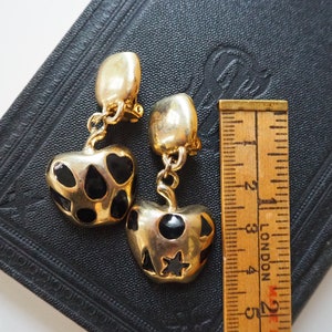 May include: A pair of gold-tone clip-on earrings with black enamel hearts and stars. The earrings are about 2 inches long.