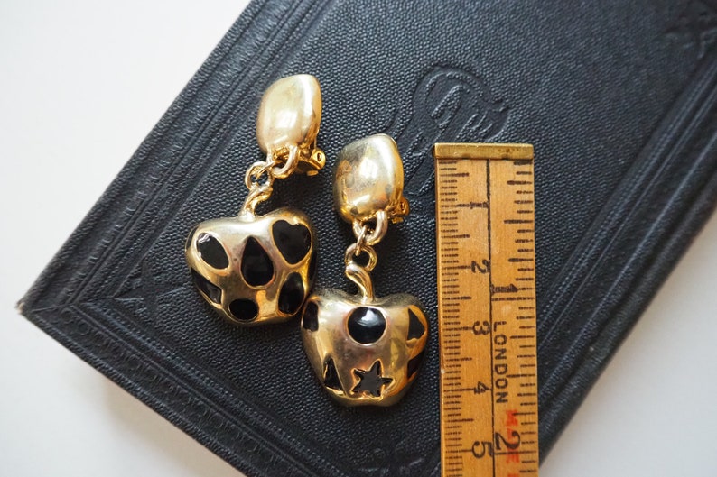 May include: A pair of gold-tone clip-on earrings with black enamel hearts and stars. The earrings are about 2 inches long.