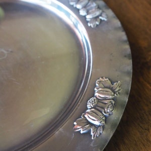 May include: A silver serving platter with a decorative embossed design of leaves and fruit around the edge.