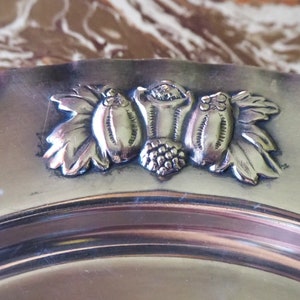 May include: A silver serving plate with a decorative design of three stylized grapes and leaves.