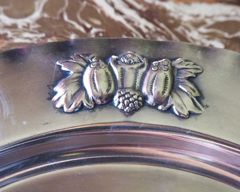 May include: A silver serving plate with a decorative design of three stylized grapes and leaves.