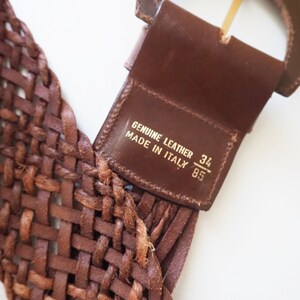 May include: A brown leather belt with a woven design and a gold buckle. The belt has a label that reads "Genuine Leather Made in Italy 34/85".